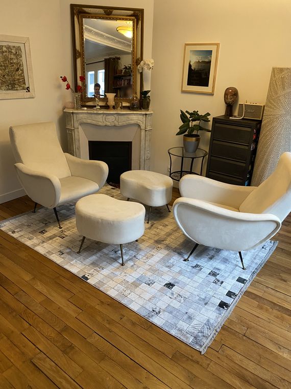 Tapis turc en soie, création d'artiste gris et blanc, posé dans un salon parisien entre deux fauteuils blancs, devant une cheminée en marbre