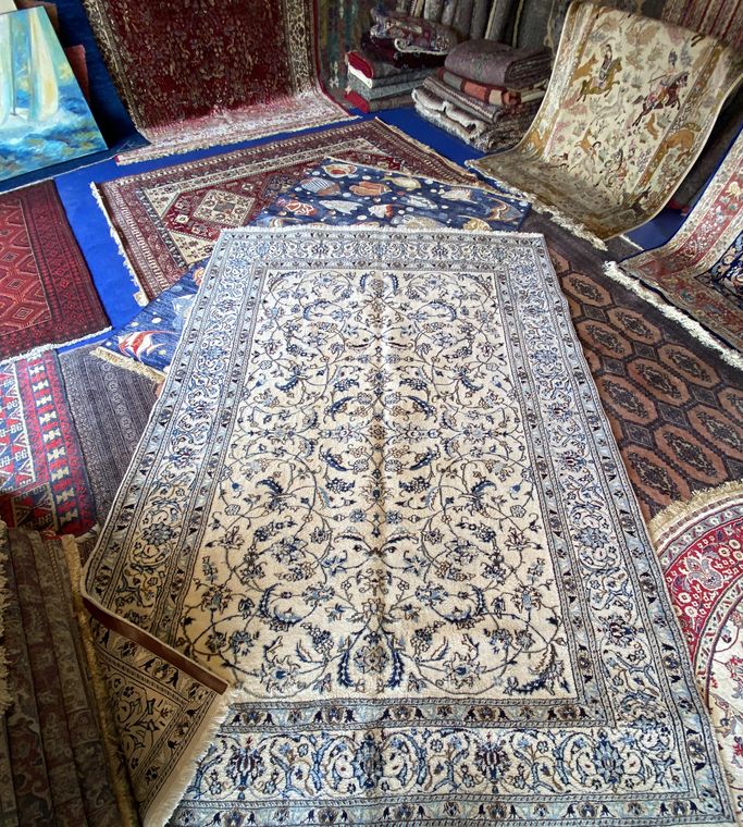 Tapis persan Naïn en laine et soie, à fond ivoire et rinceaux floraux bleus, déplié au milieu d'autres tapis de notre stock